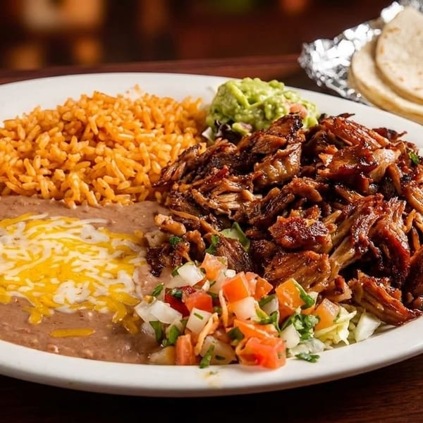 A plate of Mexican food with shredded meat, rice, refried beans, guacamole, pico de gallo, and tortillas.
