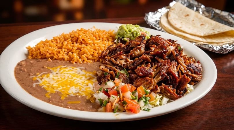 A plate of Mexican food with shredded meat, rice, refried beans, guacamole, pico de gallo, and tortillas.